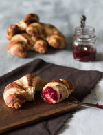 croissant mit marmelade und messer im vordergrund auf hellem untergrund.jpg