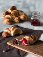 croissant mit lo?ffel auf holzbrett auf hellem untergrund.jpg